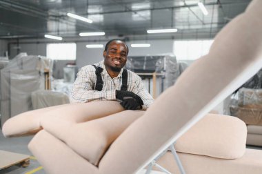 Bir mobilya fabrikasında koltukta çalışırken kameraya gülümseyen Afrikalı Amerikalı bir zanaatkar.