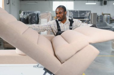 Marangoz yoğun bir mobilya fabrikasında maharetli bir şekilde bir kanepe monte ederek mobilya imalatı ve işçiliğinin karmaşık sürecini sergiliyor.