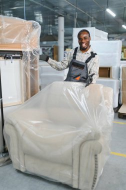 Afrika kökenli Amerikalı işçiler koruyucu plastikle bir kanepeyi hareketli bir mobilya fabrikasında ustalıkla sarıp sarmalıyor.
