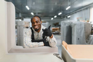 Gülümseyen Afro-Amerikan işçiler mobilya fabrikası deposunda çalışırken başparmak hareketi yapıyorlar.