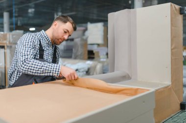 Marangoz, mobilya fabrikasında çalışırken kanepe çerçevesine koruyucu kağıt uygular. Yetenekli işçilik ve detaylara dikkat gösterir.