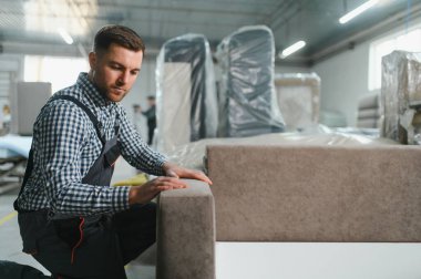 Marangoz, hareketli bir mobilya fabrikasında kanepe monte ederek döşenmiş mobilya üretiminin karmaşık sürecini gözler önüne seriyor.