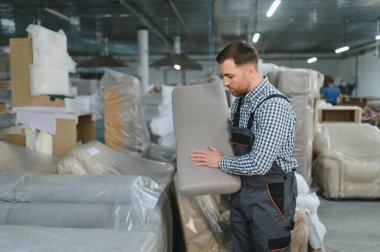 Marangoz mobilya fabrikası deposunda kanepe yastığını dikkatlice inceleyerek döşeme üretim sürecinde kalite kontrolü sağlıyor.