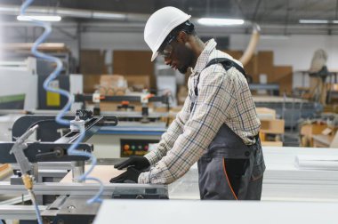 Mobilya fabrikasında cnc makinesi işleten yetenekli bir marangoz, işlemek için dikkatlice bir tahta parçası yerleştiriyor.