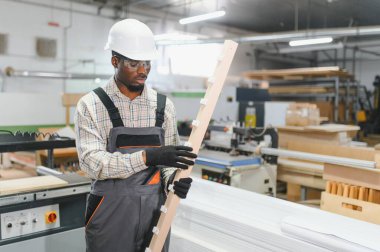 Yetenekli bir marangoz, ahşap işçiliği uzmanlığı sergileyen, hareketli bir mobilya fabrikasında uzun bir tahta parçasını inceliyor.