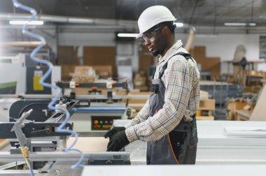 Marangoz, mobilya fabrikasında ahşap işçiliği yapan bir güvenlik ekipmanı giyiyor ve mobilya parçaları üretiyor.