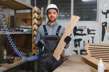 Tahta ve çivi tabancası tutan marangoz, atölyede mobilya monte etmeye hazır.