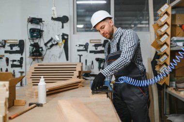 Marangoz, yoğun bir atölyede ahşap mobilya parçaları birleştirirken pnömatik çivi tabancası kullanıyor. Yetenekli işçilik ve hassasiyet sergiliyor.