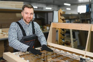 Marangoz ustalıkla ahşap bir kanepe çerçevesi ve zig zag yaylarını hareketli bir mobilya fabrikasında birleştiriyor.