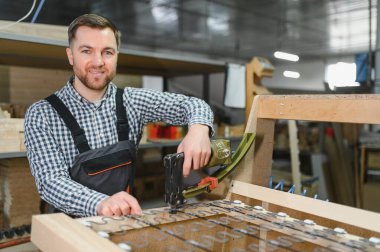 Kanepe çerçevesinde çalışan marangoz, bir mobilya atölyesindeki yayları emniyete almak için pnömatik zımba kullanıyor.