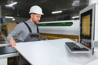 Marangoz, sandalye üretmek için bir mobilya fabrikasında ahşap tahta kesen bir makineyle çalışıyor.