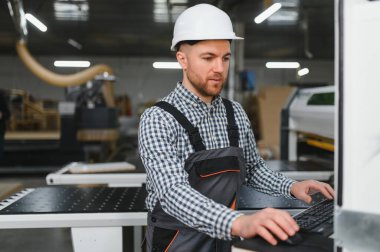 Modern bir mobilya fabrikasında güvenlik kaskı takan marangoz gelişmiş üretim süreçlerini sergiliyor.