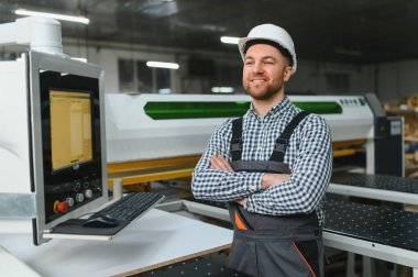 Modern fabrikada otomatik ahşap işçiliği makinesinin çaprazladığı kollarla gülümseyen kendine güvenen mobilyacı.