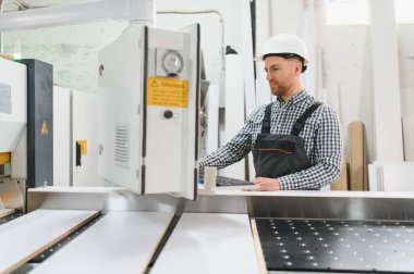 Marangoz bir mobilya fabrikasında güvenlik kaskı takıyor, kanepe üretimi için ahşap paneller kesiyor, modern marangozluk teknolojisi sergiliyor.