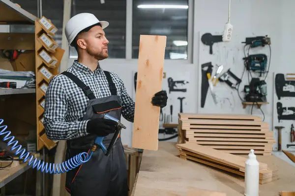 Marangoz ahşap kalasları inceliyor. Elinde pnömatik çivi tabancası var. Mobilya atölyesinde.