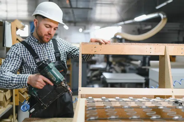 Marangoz, mobilya fabrikasında ahşap bir kanepe çerçevesi monte ederken pnömatik çivi tabancası kullanıyor.