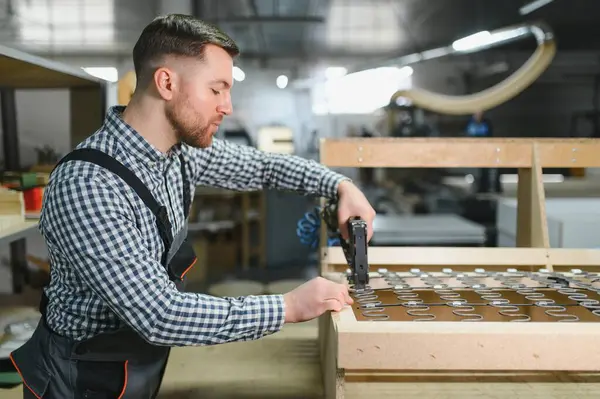 Marangoz ahşap bir kanepe çerçevesi monte ediyor. Mobilya fabrikasında pnömatik bir zımba tabancası var. Yetenekli bir işçilik ve hassasiyet sergiliyor.