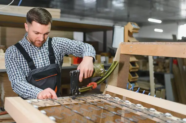 Marangoz mobilya fabrikasında çalışıyor ahşap kanepe iskeleti monte etmek için pnömatik zımba ve zig zag yayları kullanıyor.