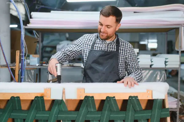 Mobilya fabrikasında pnömatik zımba kullanan bir marangoz koltuğunu döşeyip işine odaklanmış.