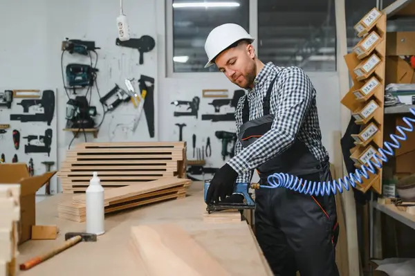 Marangoz, yoğun bir atölyede ahşap mobilya parçaları birleştirirken pnömatik çivi tabancası kullanıyor. Yetenekli işçilik ve hassasiyet sergiliyor.