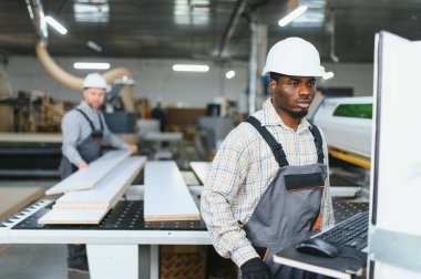 İki fabrika işçisi bir mobilya fabrikasında cnc makinesi çalıştırıyor, kanepeler ve diğer mobilyalar için ahşap parçalar üretiyorlar.