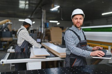 Marangozlar bir mobilya fabrikasında ahşap tahtalar keserek ahşap bir makine ile çalışıyorlar.
