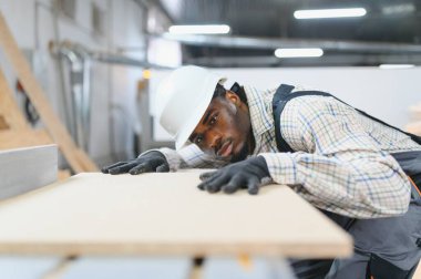 Marangoz koruyucu eldiven ve kask takıyor mobilya fabrikasında ahşap bir kalası inceliyor.