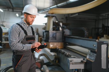 Marangoz bir mobilya fabrikasında bir cnc ahşap yönlendiriciyi kontrol ediyor, hassasiyet ve modern üretim tekniklerine odaklanıyor.