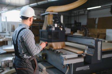 Marangoz bir mobilya fabrikasında cnc ahşap yönlendirici kontrol ediyor, gelişmiş üretim süreçlerini sergiliyor.