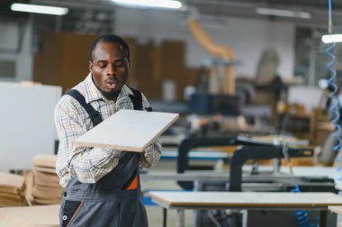 Afrika kökenli Amerikalı marangoz mobilya fabrikasında çalışırken ahşap bir tahtadan toz üflüyor.