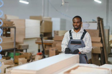 Marangoz bir mobilya fabrikasında ahşap bir kalası inceliyor, kaliteyi sağlama alıyor ve onu bir sonraki üretim aşaması için hazırlıyor.