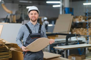 Marangoz, hareketli bir mobilya fabrikasında makinelerle çevrelenmiş bir odun parçasını gururla tutarken, marangozluk yeteneği ve kendini adamışlık sergiliyor.