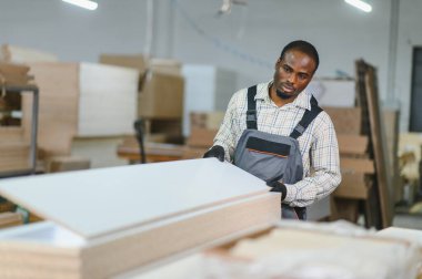 Marangoz, bir mobilya fabrikasında ahşap tahtaları taşıyarak, marangozluk ve endüstriyel üretim işleriyle uğraşıyor.