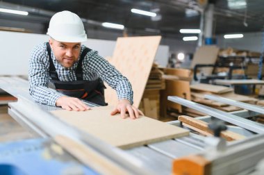 Marangoz, yoğun fabrikadaki mobilya üretimi için kesin kesinti sağlayan cnc makinesinin üzerine ahşap paneli dikkatlice yerleştiriyor.