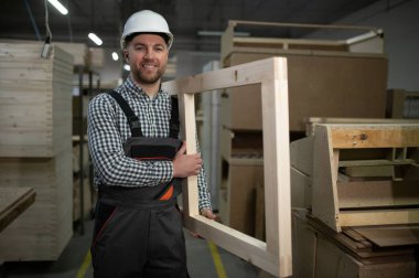 Marangoz gururla ahşap bir çerçeve tutuyor, mobilya üretimi ve tasarım sanatında olağanüstü bir zanaat sergiliyor.