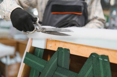 Mobilya fabrikasında çalışan bir zanaatkara yakın çekim yapmak, kanepe üretim sürecinde makasla dolgu malzemesi kesmek.