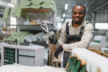 Çalışan bir mobilya fabrikasında kanepe monte etmekte usta bir zanaatkar, kalite ve konfor sağlamak için profesyonel aletler kullanıyor.