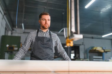 Mobilya fabrikasında otomatik kesim makinesinin yanında duran önlük giyen marangoz kanepe üretimini kontrol ediyor.