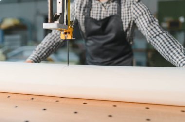 Marangoz bir mobilya fabrikasında büyük bir rulo sünger kesmek için dikey bant testeresi kullanıyor, hassasiyet ve işçiliğe odaklanıyor.