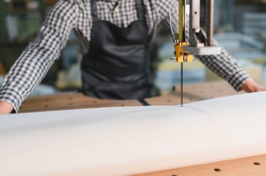 Marangoz bir mobilya fabrikasında kanepe üretimi için beyaz dolgu malzemesi kesiyor.