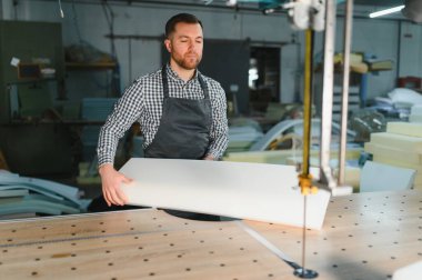 Marangoz mobilya fabrikasında köpük ve ahşap işleriyle uğraşıyor. Kanepe üretimi için malzeme hazırlıyor.