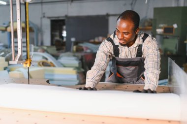 Marangoz elektrikli testere kullanıyor. Mobilya fabrikasında kumaşı ustalıkla kesiyor. Sanatçılık ve hassasiyet sergiliyor.