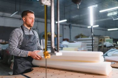 Marangoz, mobilya fabrikasındaki bir testereyle ustalıkla köpük keserek imalat işlemi için özel yapım koltuklar yaratıyor.