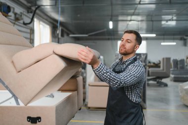 Marangoz mobilya fabrikasında kanepe monte ederek döşenmiş mobilya işçiliğinin karmaşık üretim sürecini vurguluyor.