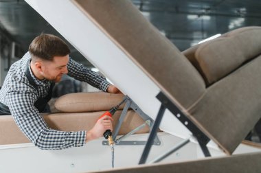 Mobilyacı, pnömatik bir tornavida kullanarak mobilya fabrikasında kanepe çerçevesi kuruyor. Yetenekli bir işçilik sergiliyor.