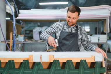 Bir mobilya fabrikasında çalışan marangoz kanepeyi monte etmek için zımba tabancası kullanıyor, işçilik ve üretim sürecine odaklanıyor.
