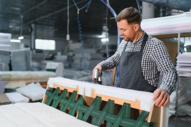 Marangoz pnömatik zımba tabancasını ustalıkla kullanıyor, mobilya fabrikasında bir kanepenin ahşap çerçevesini birleştiriyor.