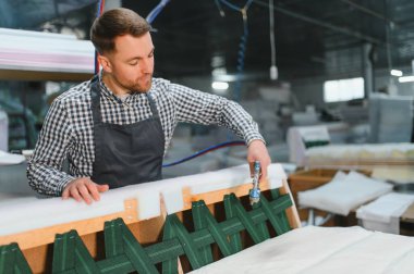 Marangoz ahşap kanepe çerçevesine ağ örmek için pnömatik zımba tabancası kullanır, fabrikada mobilya üretimi üzerinde çalışır.
