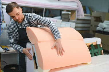 Marangoz bir mobilya fabrikasında kanepe monte ediyor. Kauçuk ve ahşapla ustalıkla çalışarak kaliteli el yapımı parçalar yapıyor.