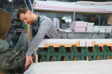 Marangoz, mobilya fabrikasında ustalıkla döşeme üzerinde çalışırken kanepe çerçevesinde kayışları emniyete alıyor.